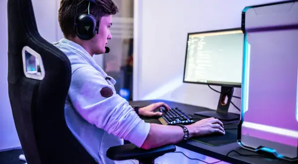 Ein junger Mann mit Headset spielt am PC. Er fragt sich vielleicht, was bedeutet gg im Chat.