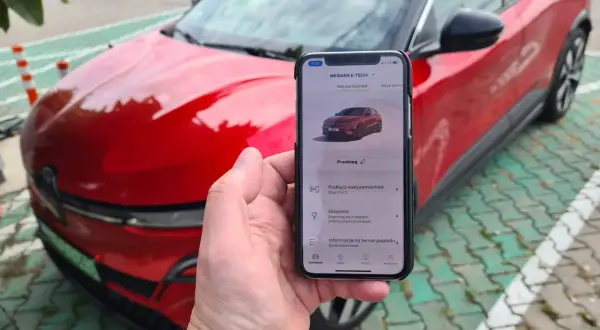 Aplikacja na telefonie pokazuje, jak przerobić auto na elektryczne, obok czerwonego samochodu.