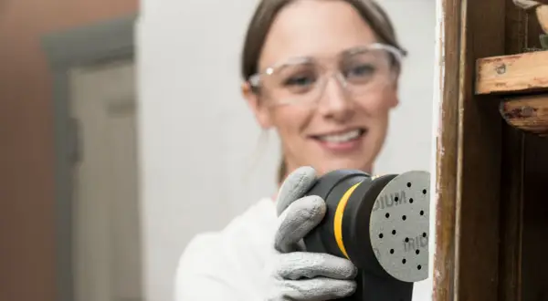 Mujer con gafas de seguridad usa lijadora orbital para restaurar madera, una forma eficiente de como lijar madera sin lija.
