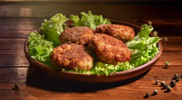 Cztery apetyczne kotlety mielone, idealnie wysmażone w airfryer, podane na liściach sałaty.