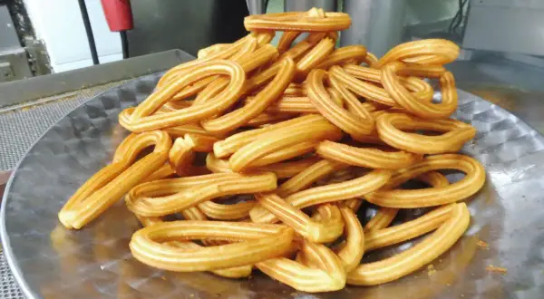 Montón de churros dorados en forma de lazo sobre un plato metálico.