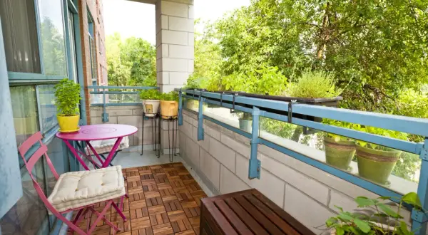 Zielony balkon z meblami i roślinami. Jak osłonić balkon w bloku? Rośliny na balustradzie i drewniana podłoga dodają uroku.