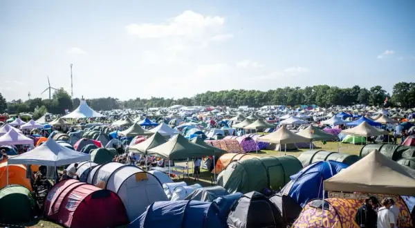 Ein Meer von Zelten beim Roskilde Festival. Menschen entspannen sich im Freien unter blauem Himmel, umgeben von bunten Unterkünften.