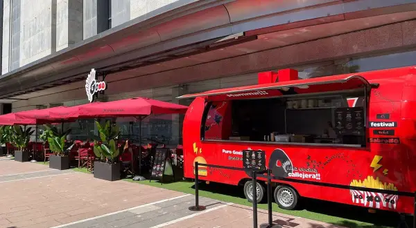 Food truck rojo "Puro Goxis" de Dabiz Muñoz, con "Mamma!!!" y "Alta cocina callejera!!" escrito. Mesas y sombrillas rojas al lado.