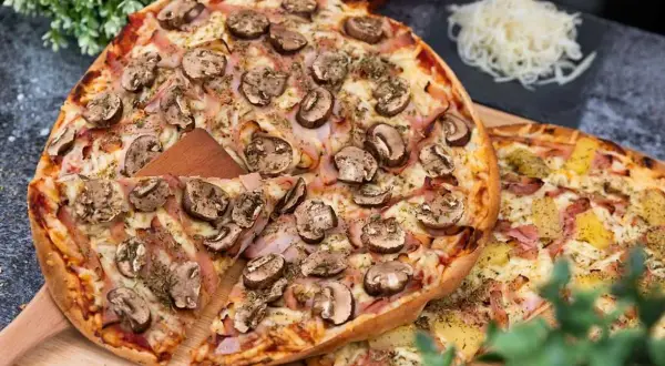 En härlig liba pizza med champinjoner och skinka, redo att avnjutas. Bredvid ligger en annan pizza med ananas och skinka.