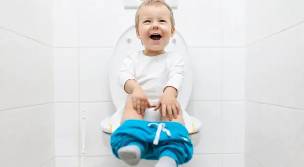 Bambino felice sul water, pantaloni abbassati, pronto per la sua prima cacca nel water.