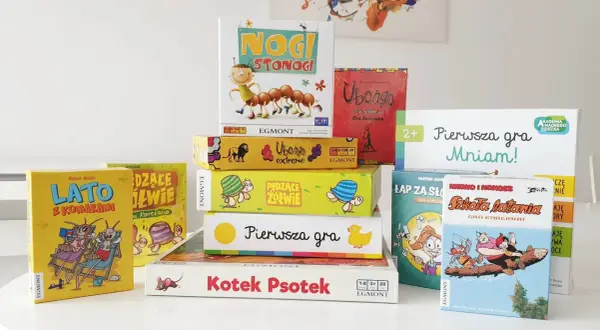 Stos kolorowych pudełek z grami planszowymi, idealnych na szybkie gry planszowe. Widać m.in. "Nogi Stonogi", "Ubongo" i "LATO z Komarami".