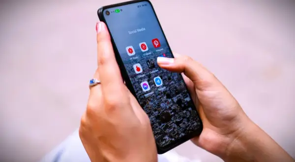 Dłonie trzymają telefon z ikonami aplikacji społecznościowych. Zastanawiasz się, jak trwale usunąć wiadomości z Messengera?