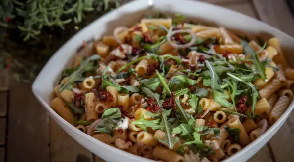 Ein köstlicher nudelsalat mit getrockneten tomaten, Rucola und Mozzarella in einer weißen Schüssel.