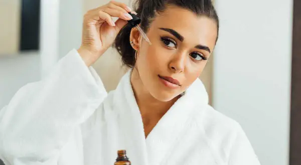 Une femme applique un sérum sur son visage, peut-être un mélange d'acide azélaïque et de vitamine C, pour une peau éclatante.