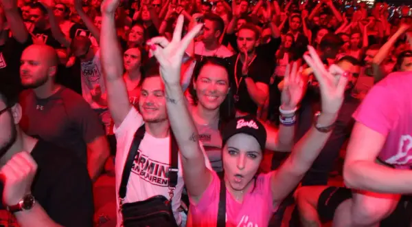 Tłum na koncercie Armin van Buuren Polska, fani pozdrawiają DJ-a, czerwone światła tworzą energetyczną atmosferę.