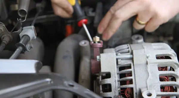 Dłonie mechanika odkręcają śrubę przy alternatorze samochodu.