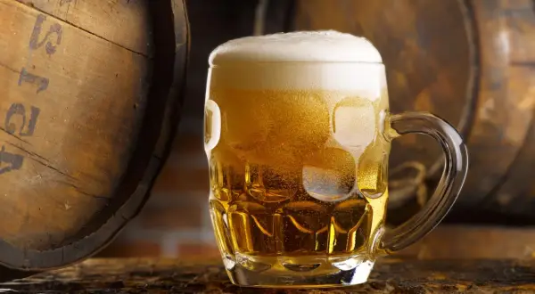 Boccale di birra dorata con schiuma, accanto a botti di legno. Un litro di birra calorie da gustare con moderazione.