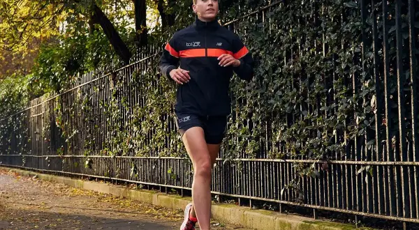 Kobieta w sportowym stroju biegnie po chodniku. Idealny przykład, jak się ubrać do biegania jesienią: lekka kurtka, spodenki i buty.