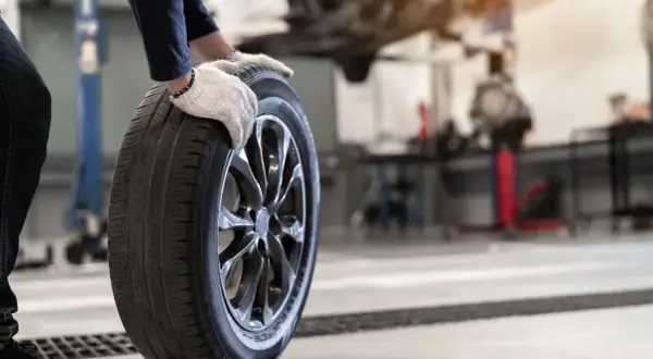 Mechanik w rękawiczkach trzyma oponę. Czy opony rowerowe do miasta z gładkim bieżnikiem zużywają się szybciej na kostce i asfalcie?