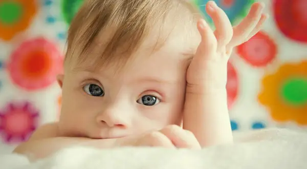 Bambino con sindrome di Down, occhi azzurri, mano sul viso. La vita delle persone Down è piena di amore e gioia.
