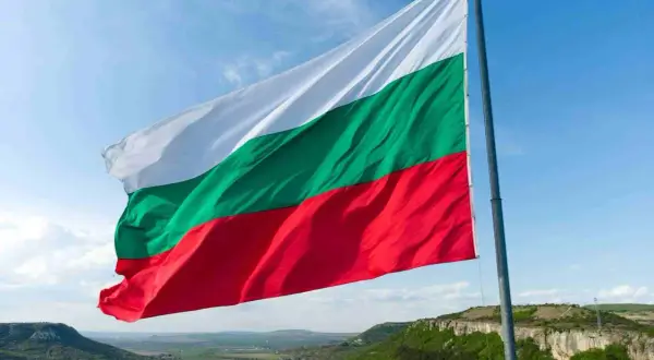 Flaga Bułgarii powiewa na tle błękitnego nieba nad malowniczym krajobrazem. Winieta Bułgaria.