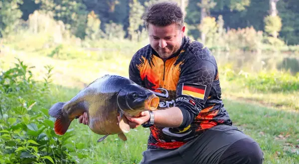 Wędkarz z dumą prezentuje okazałego karpia, który z pewnością nie jest ani sieją, ani sielawą.