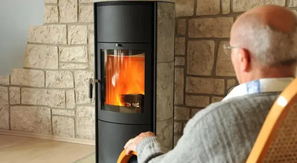 Älterer Mann sitzt vor einem brennenden Kaminofen. Die Idee, den Kamin stilllegen, kommt auf, wenn man ihn nicht mehr braucht.
