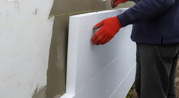 Pracownik w czerwonych rękawicach montuje styropian na elewacji. Zastanawiasz się, ile za metr tynku na elewacji?