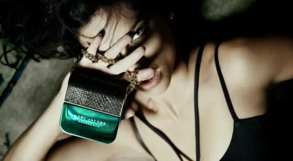Kobieta zmysłowo liże palec, trzymając w dłoni flakon perfum Marc Jacobs Decadence.