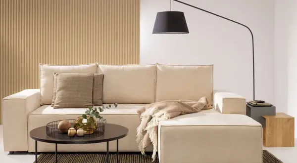Salon z aneksem bez okna. Jasna kanapa, stolik kawowy, lampa łukowa i dekoracje tworzą przytulną atmosferę.