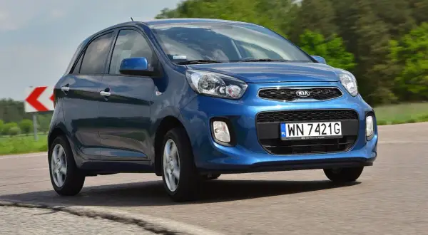 Niebieski Kia Picanto 2012 na drodze, z zielonymi drzewami w tle.
