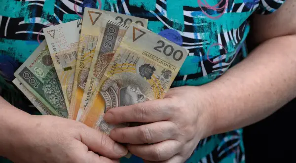 Dłonie trzymają polskie banknoty 100 i 200 zł. Może to być pomoc finansowa, np. specjalny zasiłek opiekuńczy.