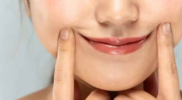 Dłonie delikatnie unoszą opadające kąciki ust, próbując nadać im uśmiech.