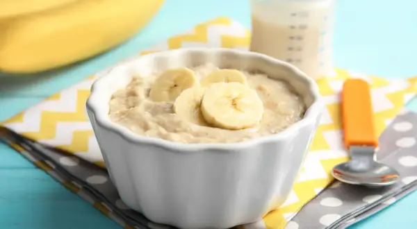 Ein Schüsselchen mit Bananen-Abendbrei, perfekt zum abendbrei selber machen. Daneben eine Babyflasche und ein Löffel.