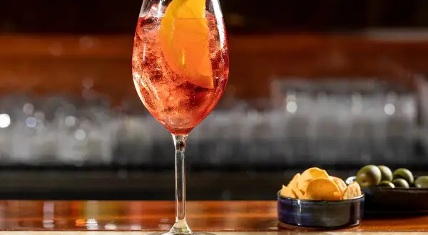 Un bicchiere di Spritz con fetta d'arancia, ghiaccio e stuzzichini. La spritz ricetta perfetta per l'aperitivo.