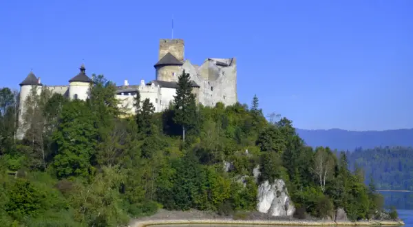 Zamek w Niedzicy, majestatyczna twierdza na wzgórzu, otoczona zielenią, z widokiem na jezioro i góry.