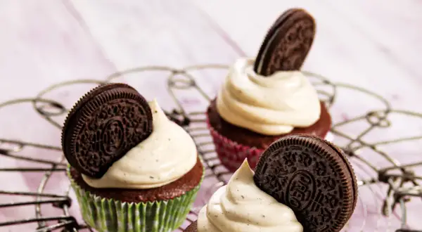 Drei leckere Oreo Muffins mit cremiger Glasur und einem Oreo-Keks obendrauf, auf einem Gitterrost arrangiert.
