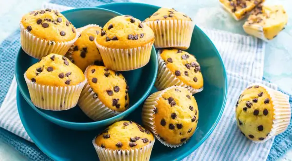 Muffin con gocce di cioccolato, dorati e invitanti, serviti in una ciotola blu.