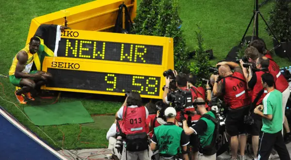 Usain Bolt, najszybszy człowiek świata, świętuje nowy rekord świata 9.58s. Otoczony przez fotoreporterów, z flagą Jamajki.