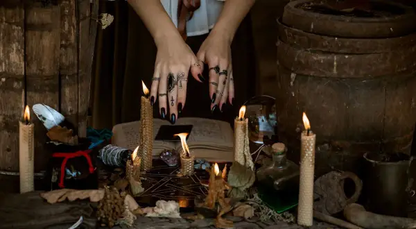 Dłonie z pierścieniami i tatuażami symbolizującymi symbole słowiańskie i ich znaczenie, otoczone płonącymi świecami i magicznymi przedmiotami.