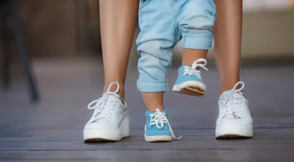 Dziecko w niebieskich bucikach i dorosły w białych sneakersach na drewnianym tarasie.