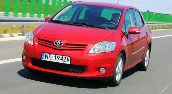 Czerwony Toyota Auris 2010 jedzie autostradą. Kierowca w czapce prowadzi auto.