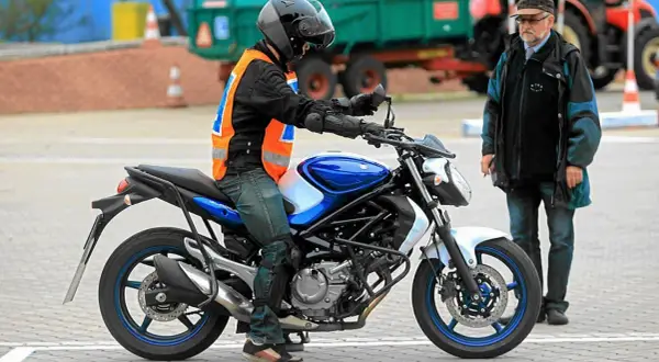 Młody motocyklista w kamizelce odblaskowej na placu manewrowym, obok instruktor. Zastanawia się, od ilu lat prawo jazdy jest wymagane na motocykl.
