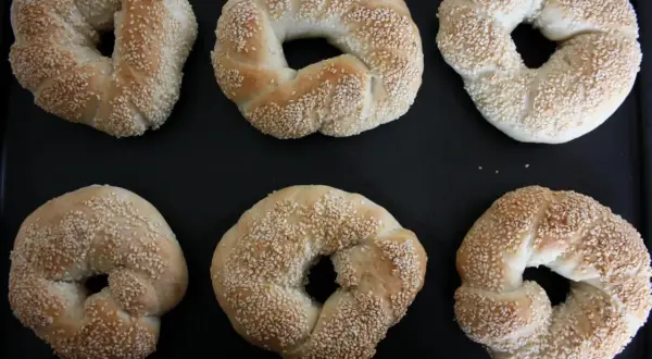 Sex gyllene simit, täckta med sesamfrön, ligger på en svart plåt. Perfekt för ett simit recept!