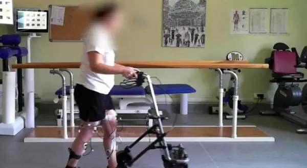 Persona con invalidità cammina con deambulatore, sensori alle gambe per neurostimolatore midollare.