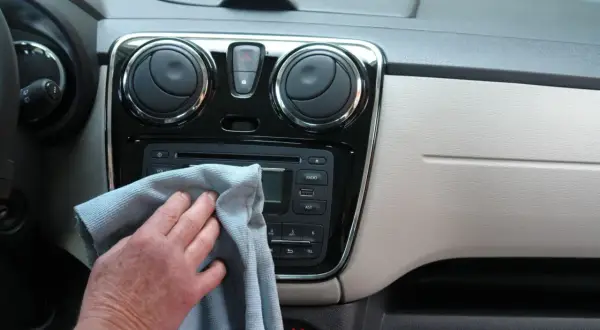 Ręka z szarą ściereczką czyści radio samochodowe i nawiewy. Dbałość o mycie detali w aucie.