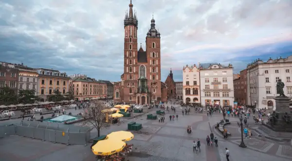 Rynek Główny w Krakowie, z Bazyliką Mariacką w centrum, to jeden z krakowskich top attractions. Ludzie spacerują, a żółte parasole tworzą barwne plamy.