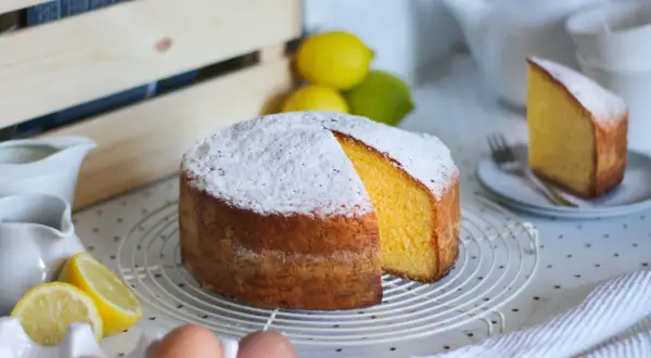 Una torta paradiso sofficissima, cosparsa di zucchero a velo, con spicchi di limone e uova fresche.