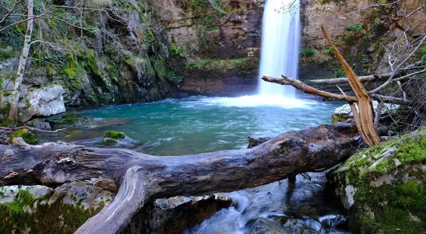 Impresionantes cascadas en Galicia, con un tronco caído en primer plano y aguas turquesas.