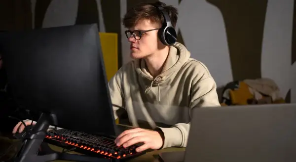 Młody mężczyzna w słuchawkach i okularach pracuje przy komputerze. Czy technik programista jest trudny? To zależy od pasji i zaangażowania.