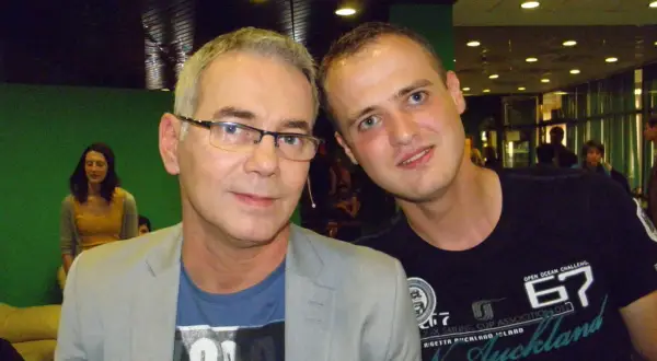 Dwóch mężczyzn pozuje do zdjęcia. Starszy, w okularach i jasnej marynarce, zastanawia się, czy prowadzący naprawdę zna wszystkie piosenki, czy korzysta z promptera.