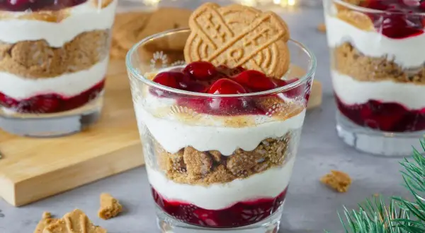 Festliche Desserts im Glas mit Kirschen, Kekskrümeln und Sahne, garniert mit Spekulatius.
