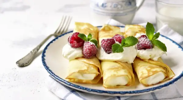 Pyszne naleśniki z mascarpone, udekorowane malinami i miętą, czekają na talerzu. Idealny deser na każdą okazję.