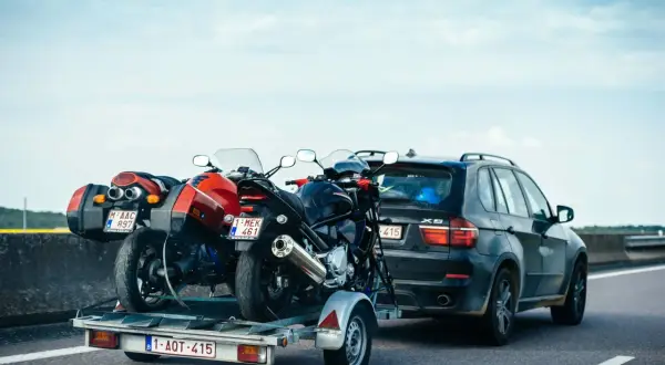 Deux motos sur une remorque tirée par une voiture sur l'autoroute. Le transport de ces véhicules nécessite un permis adéquat pour la catégorie de véhicule tracté.